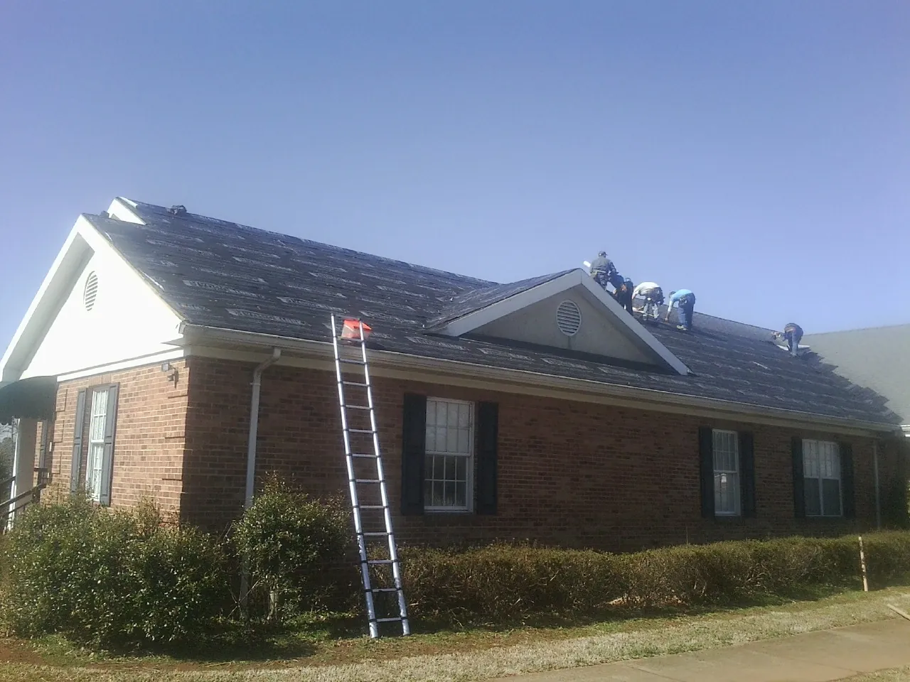Crew tearing shingles off a brick ranch roof with a ladder set — Metal Roof Repair work by our crew in Cropseyville