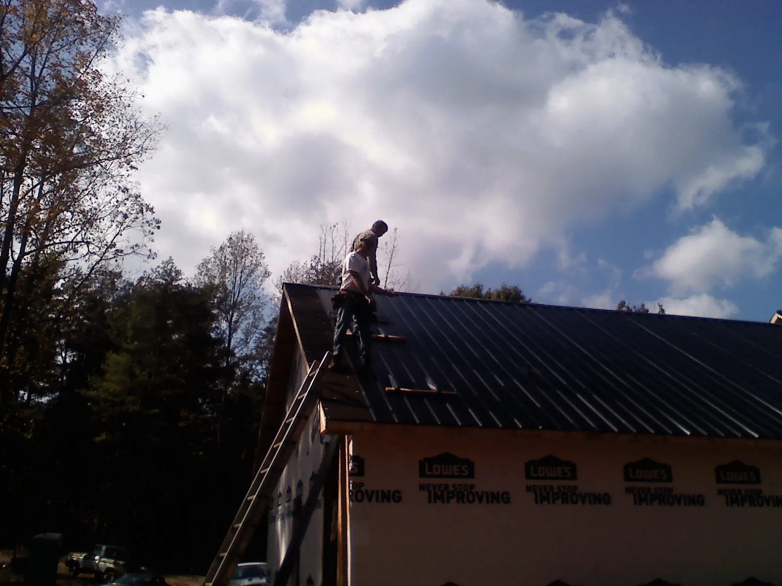 Roofer fastening dark metal panels high against a cloudy sky, from a Roof Inspection job in Cropseyville