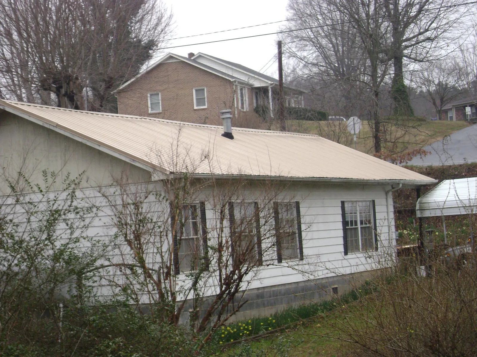 Tan metal roof on a white sided house set into a hillside — Commercial Roofing by Roofing Brothers in Cropseyville